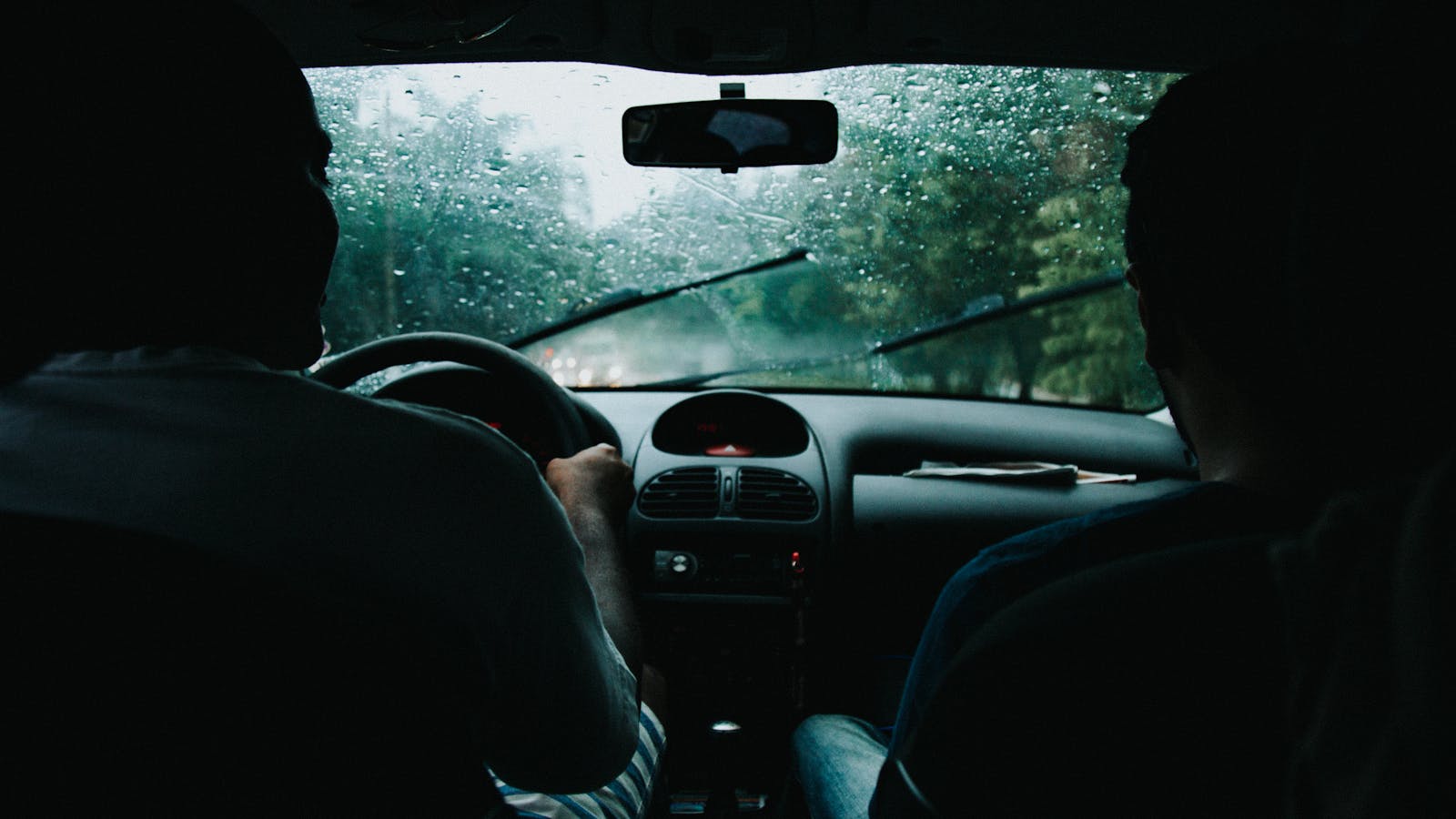 Two people drive auto through rainy São Paulo streets, wet windshield and raindrops visible.